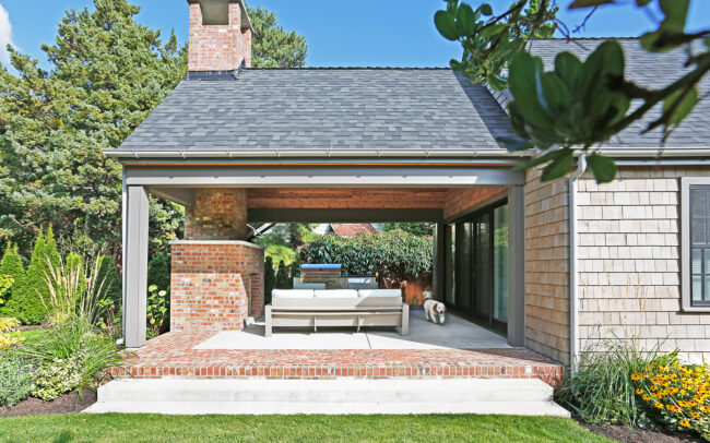 The covered patio with a brick fireplace, outdoor furniture and grill.