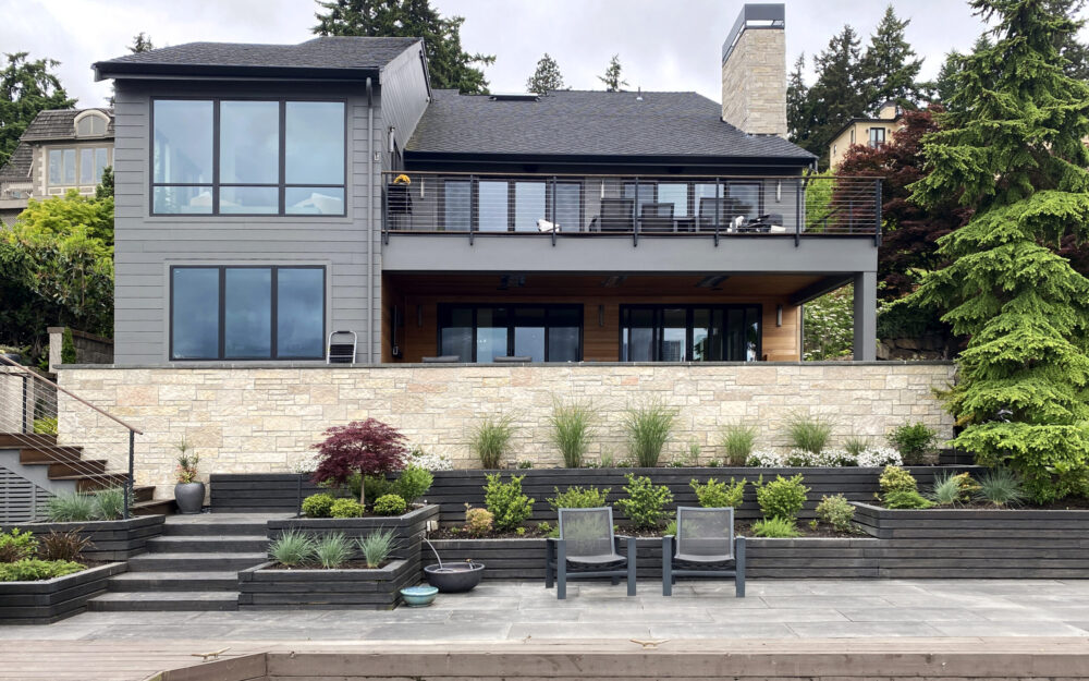 The back of the house with a covered patio on the lower level and an open deck on the main floor. A pathway along cascading planters leading to the boat dock.