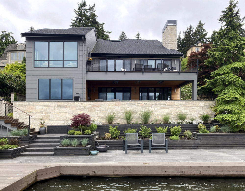 The back of the house with a covered patio on the lower level and an open deck on the main floor. A pathway along cascading planters leading to the boat dock.